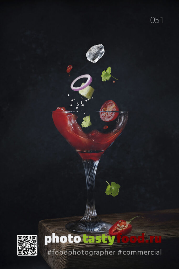 Гаспачо, включая лук, лед, помидоры и кинзу, на темном фоне. A Bloody Mary cocktail in a glass with floating garnishes, including onion, ice, tomato, and cilantro, against a dark background. Фуд фотограф | food photographer